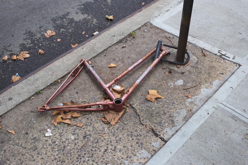 A red bicycle completely stripped down to the frame lying locked to a post.