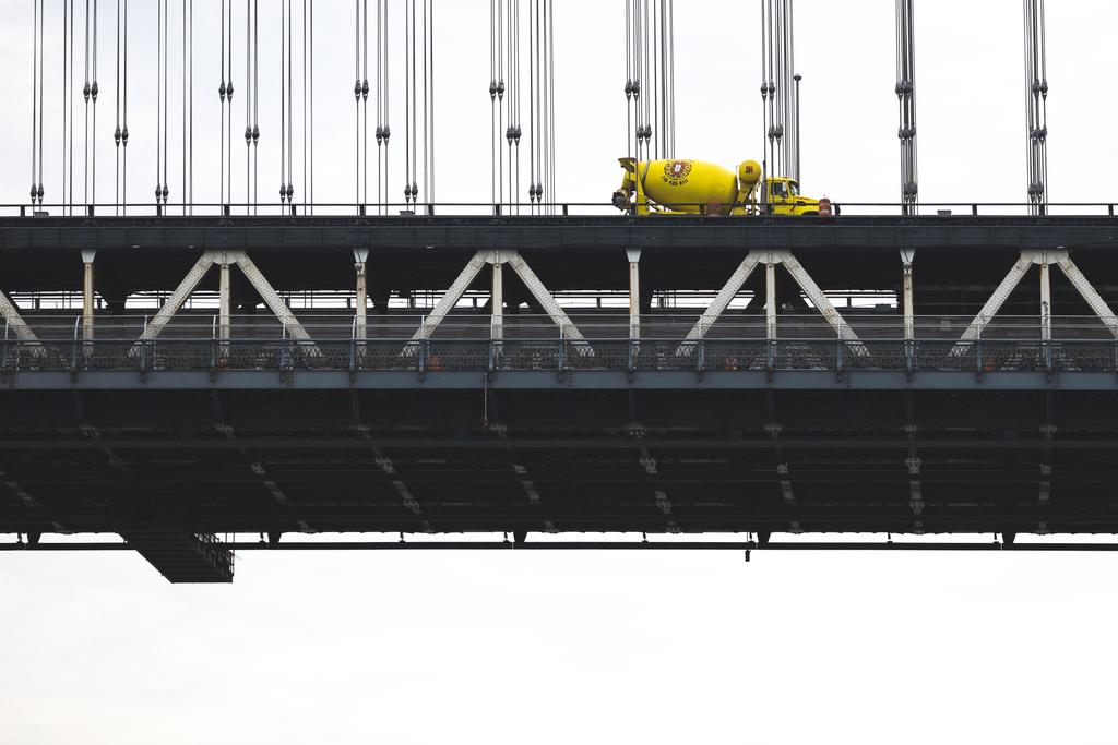 A bright yellow cement mixer crossing the Manhattan suspension bridge in the distance, viewed from Dumbo.
