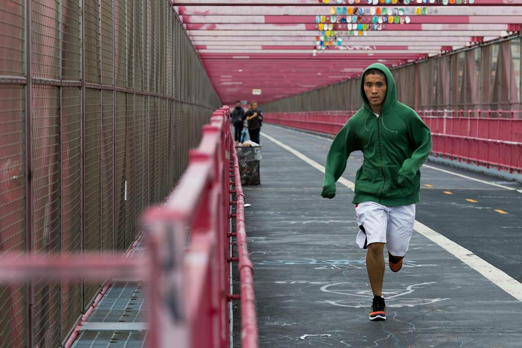 A man in a green hoodie and shorts jogs towards me over the Williamsburg Bridge.